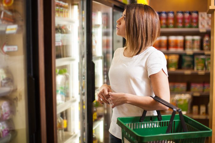 Beautiful young brunette doing some shopping at a supermarket and looking at a refrigerator