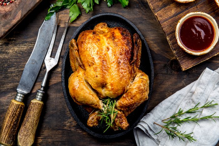 Roasted chicken with rosemary served on black plate with sauces on wooden table, top view