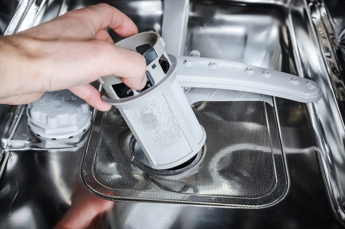 Maintenance of home appliances. Man cleans the filter in the dishwasher.