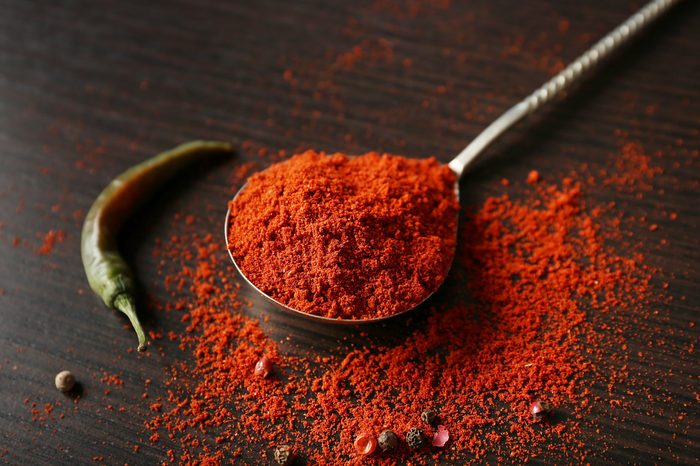 Spoon with paprika powder and chili pepper on wooden background