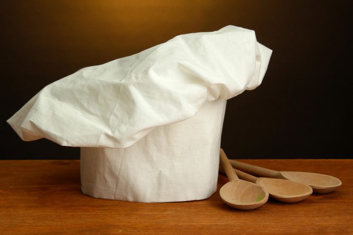Chef's hat with spoons on table on brown background