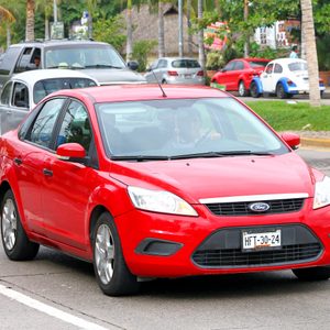 Red Ford car driving on a multi-lane road, surrounded by other vehicles and palm trees; license plate reads 