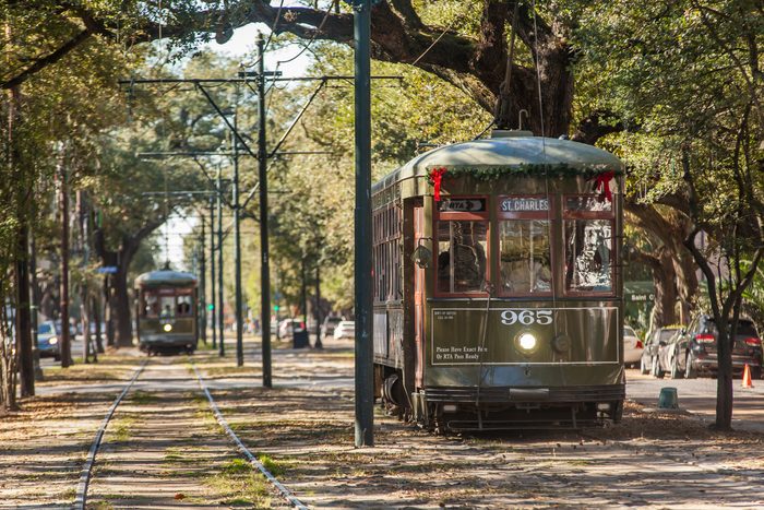 A green streetcar travels along a tree-lined track. The destination sign reads 
