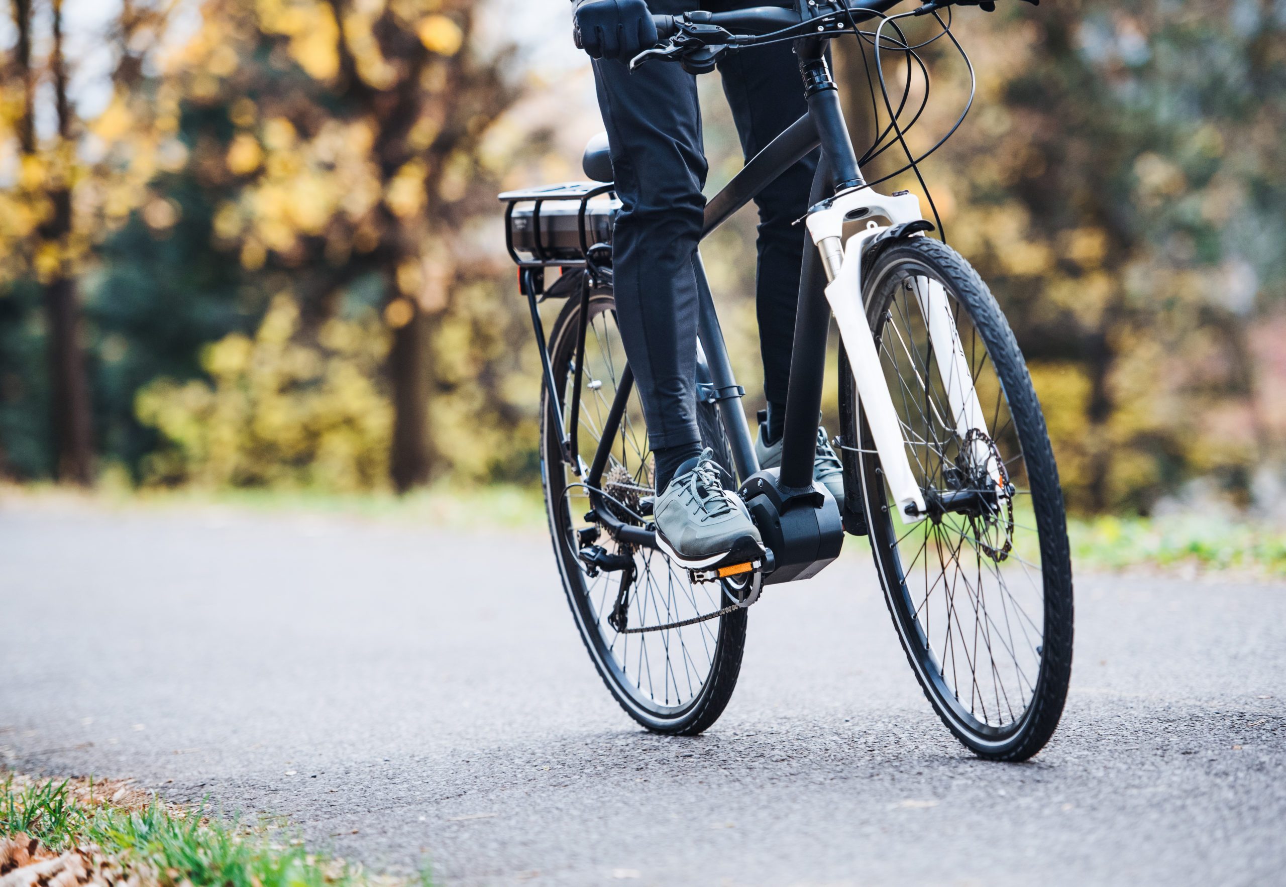 An unrecognizable man on electrobike cycling outdoors on a road in park.