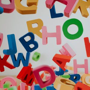 Colorful wooden letters fall against a plain background, scattering chaotically, creating a playful and dynamic scene.