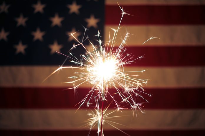 Lit sparkler in front the American Flag for 4th of July celebration
