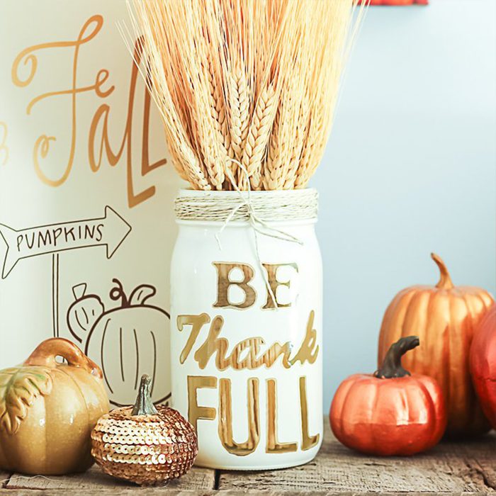 Jar holds wheat stalks on wooden surface. Text reads, 