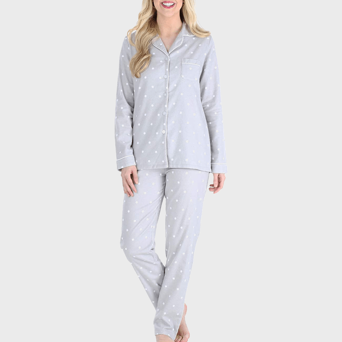 Person wearing gray polka-dot pajamas stands against a plain white background, smiling with arms relaxed by their sides.