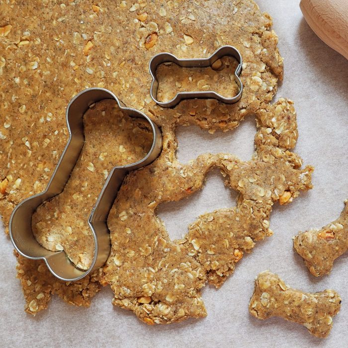 Bone-shaped cookie cutters create treats from dough on parchment paper, accompanied by a wooden rolling pin.