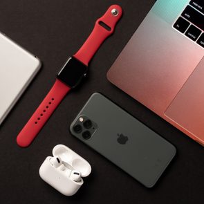 Various Apple devices, including a laptop, smartphone, smartwatch, and earbuds, are displayed on a dark surface in a minimalist arrangement.