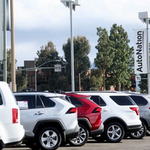 Cars parked in a dealership lot, surrounded by trees and street signs, with banners displaying 