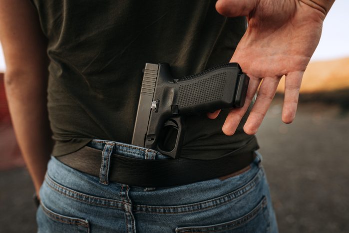 Hand of a man reaching for a gun hidden behind his back.