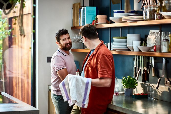 Cheerful male couple washing up together in kitchen