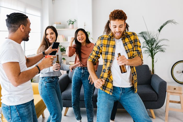Multi ethnic group of young student friends dancing and celebrating together while having party at home