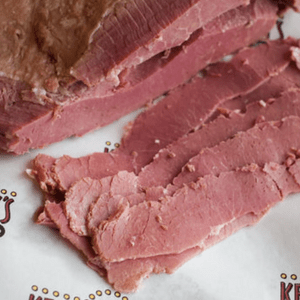 Slices of corned beef are neatly piled on white deli paper, creating a rustic presentation.