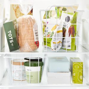 Plastic bins organize food packages and containers in a refrigerator, featuring bags of vegetables, bread, and ice cream tubs neatly arranged on two shelves.