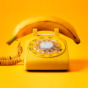 Yellow rotary phone with a banana resting on top, set against a matching yellow background.