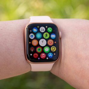 Smartwatch displaying colorful app icons, worn on a person's wrist, against a blurred green outdoor background.