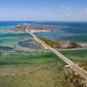 Road stretches across a series of small islands and turquoise waters under a clear blue sky, linking distant landmasses.