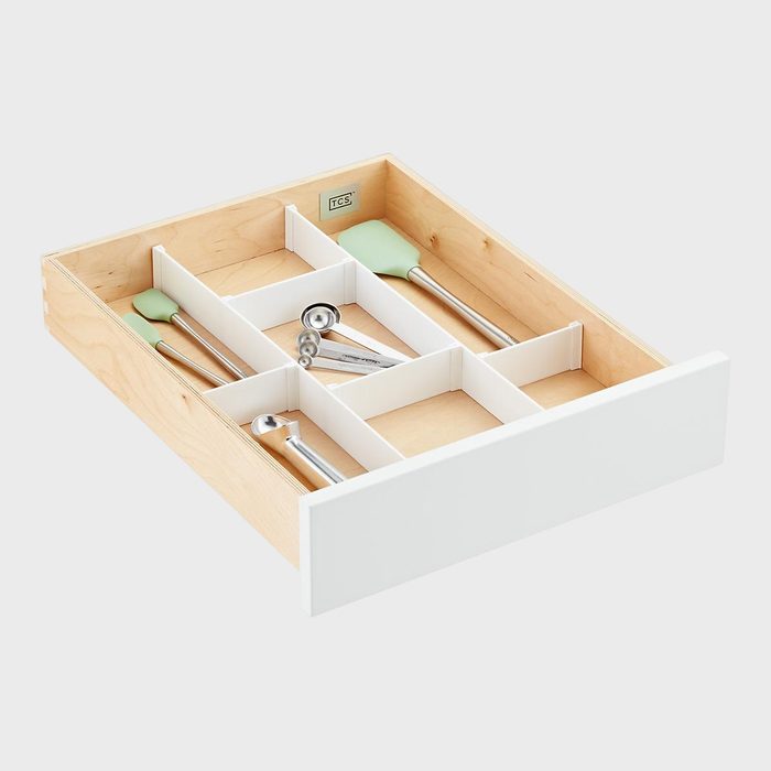 Wooden drawer with white dividers arranging kitchen tools, including spatulas and measuring spoons, in a neatly organized, minimalist setting.