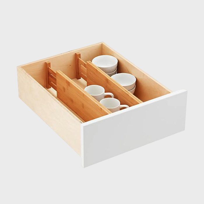 Wooden drawer with dividers organizes cups and bowls, set against a plain background.