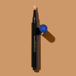 Black cosmetic pen with beige tip lies on a brown surface; blue cap detached, showing text 