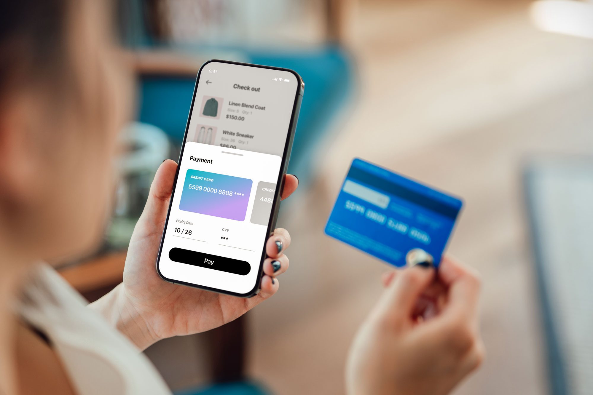 A person holds a phone displaying an online checkout screen and a credit card, indicating an online shopping transaction in progress.