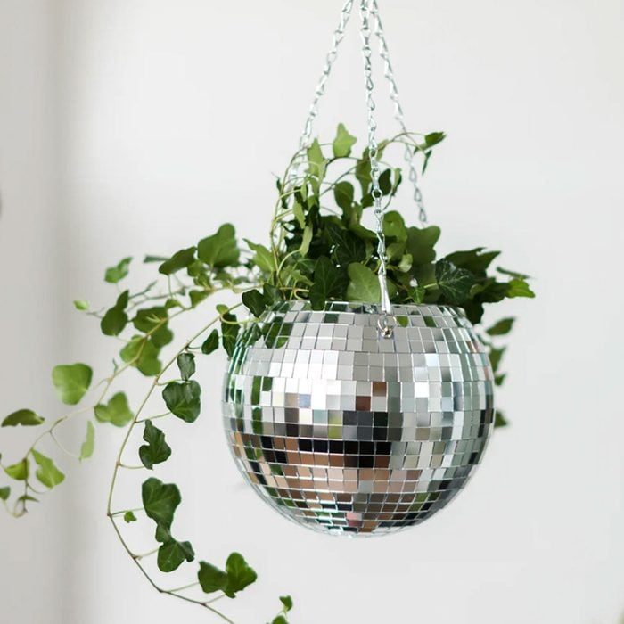 A mirrored disco ball planter hangs, filled with cascading green ivy, against a plain white background.