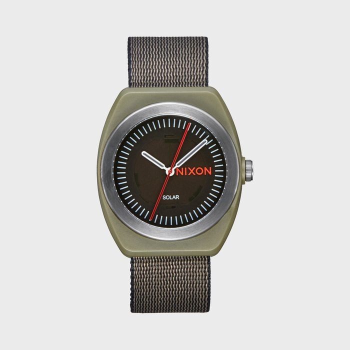 Watch displaying time, resting on a plain surface, featuring a dark face, white and red hands, brown strap. Text: 