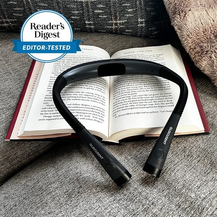 Book lies open, illuminated by a flexible neck reading light, on a cozy couch. 