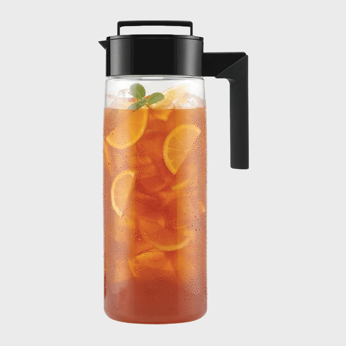 A clear pitcher holds iced tea with lemon slices and mint, on a plain background.
