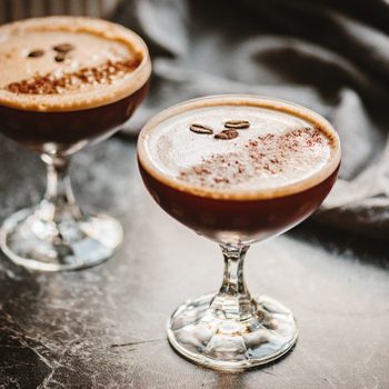 Two espresso martinis with three espresso beans on top, on a black marble countertop