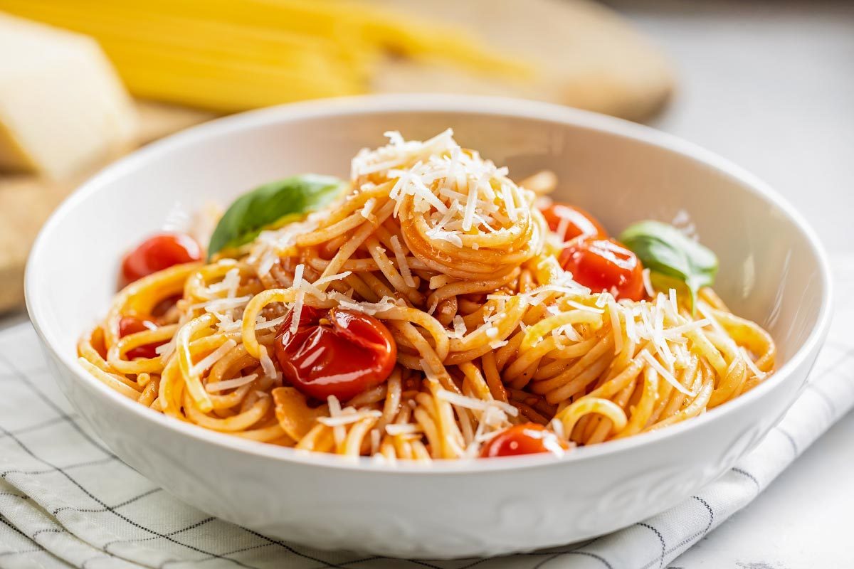 Plate with spaghetti in tomato sauce, parmesan cheese and basil.
