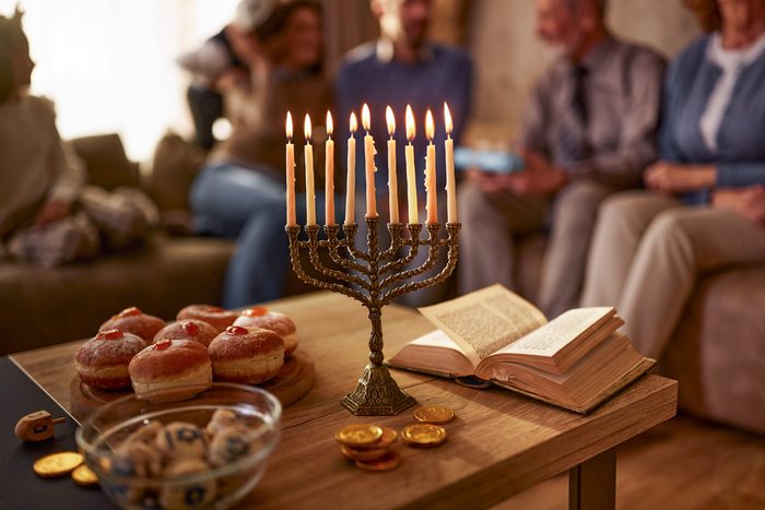 Close up of menorah with traditional food and Torah for Hanukkah with extended family in the background.